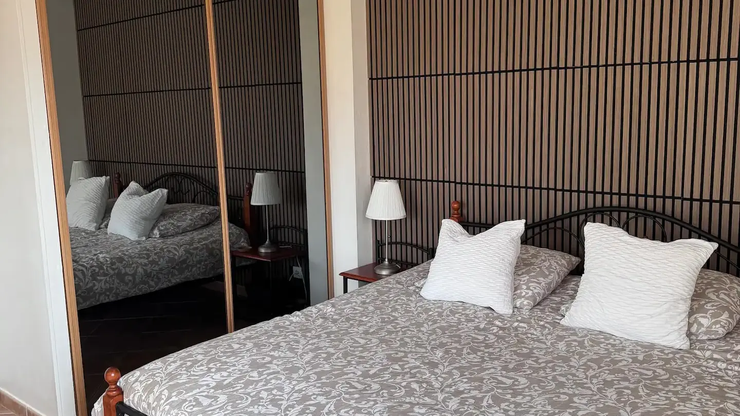 Partie chambre avec un grand lit au cadre en fer forgé, doté d'une tête de lit et d'un placard à portes coulissantes en miroir.