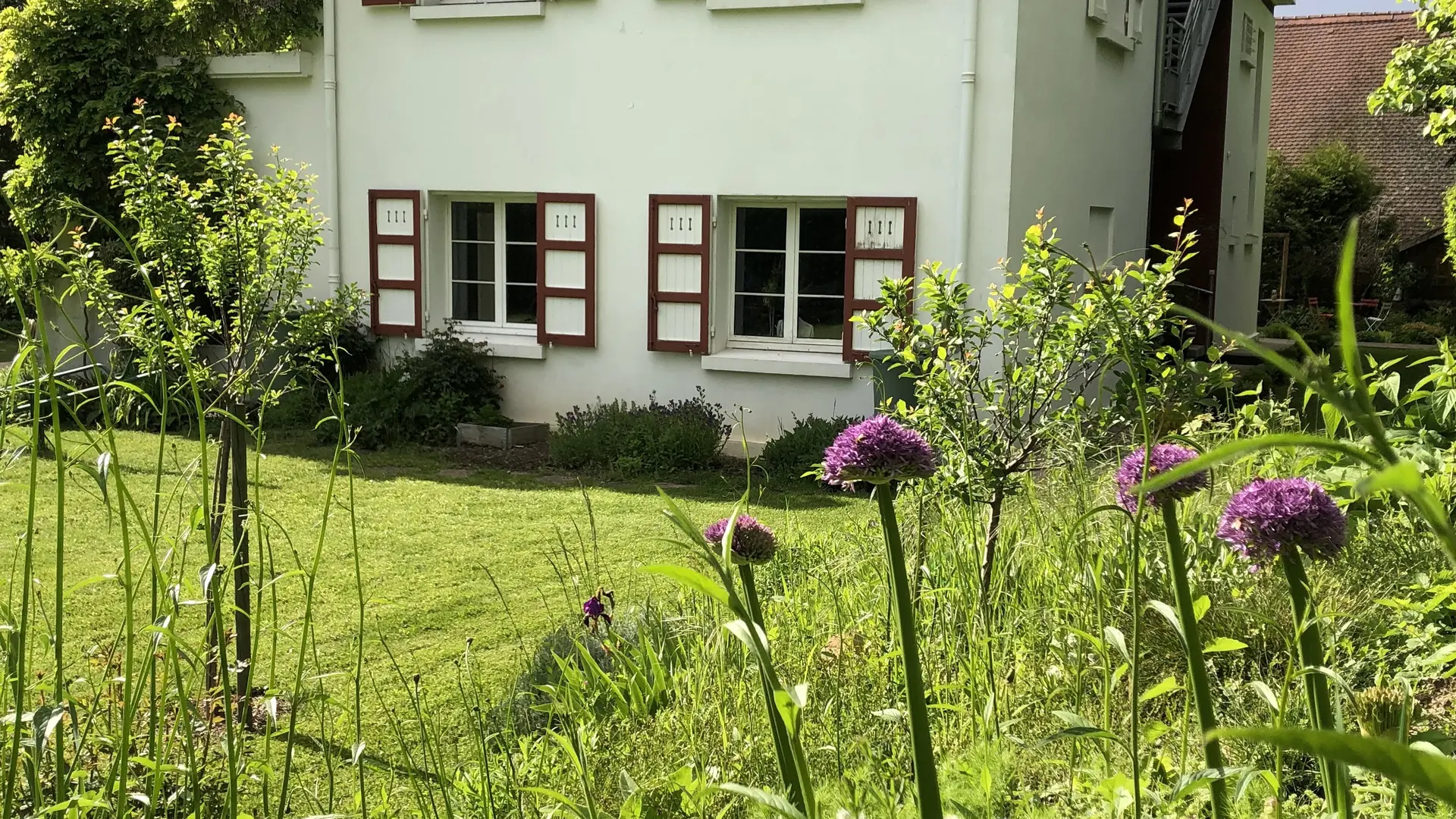 Cette façade est constituée d'un bâtiment à colombages, avec des murs blancs et des poutres en bois apparentes de couleur rouge. Un jardin arboré se trouve devant le bâtiment.