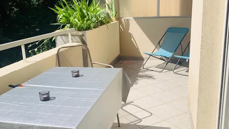 Terrasse carrelée avec une table, deux chaises et deux chaises longues.