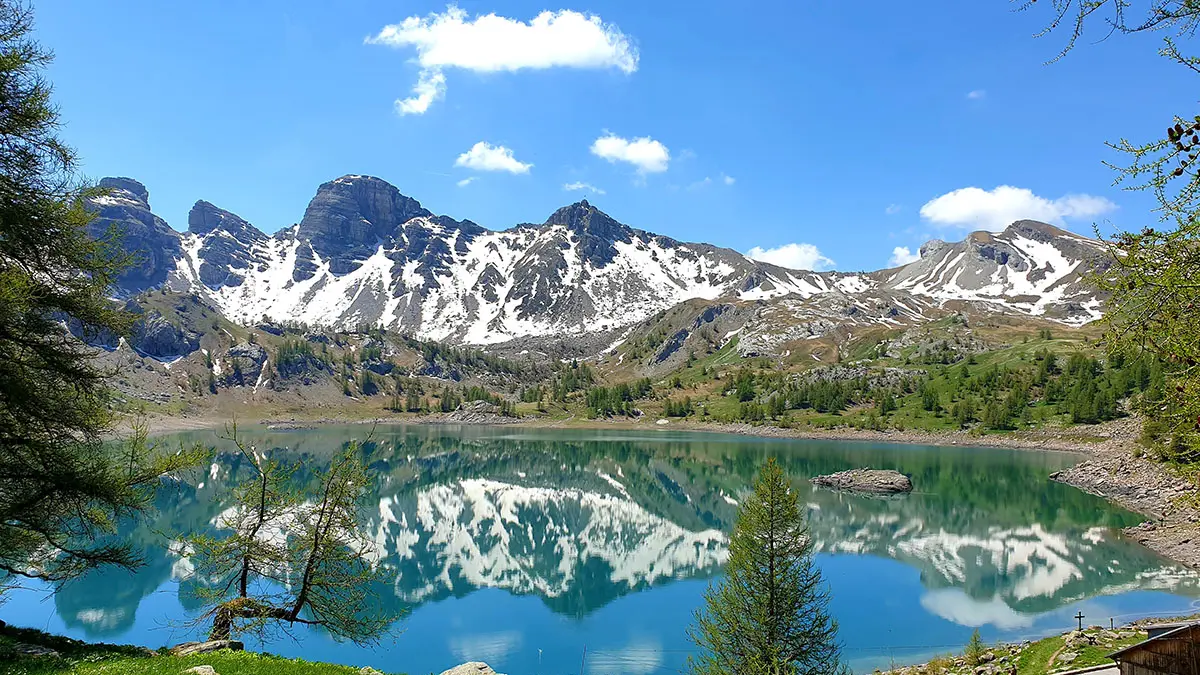 Le Lac d'Allos en fin de printemps, végétation verdoyante autour du lac, montagnes dites têtes du Lac en arrière-plan avec neige subsistante