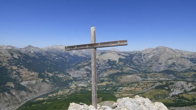Croix de bois située au sommet de la montagne de Rochecline, sur un tas de cailloux. Vue complètement dégagée du village d'Allos et des montagnes en contrebas
