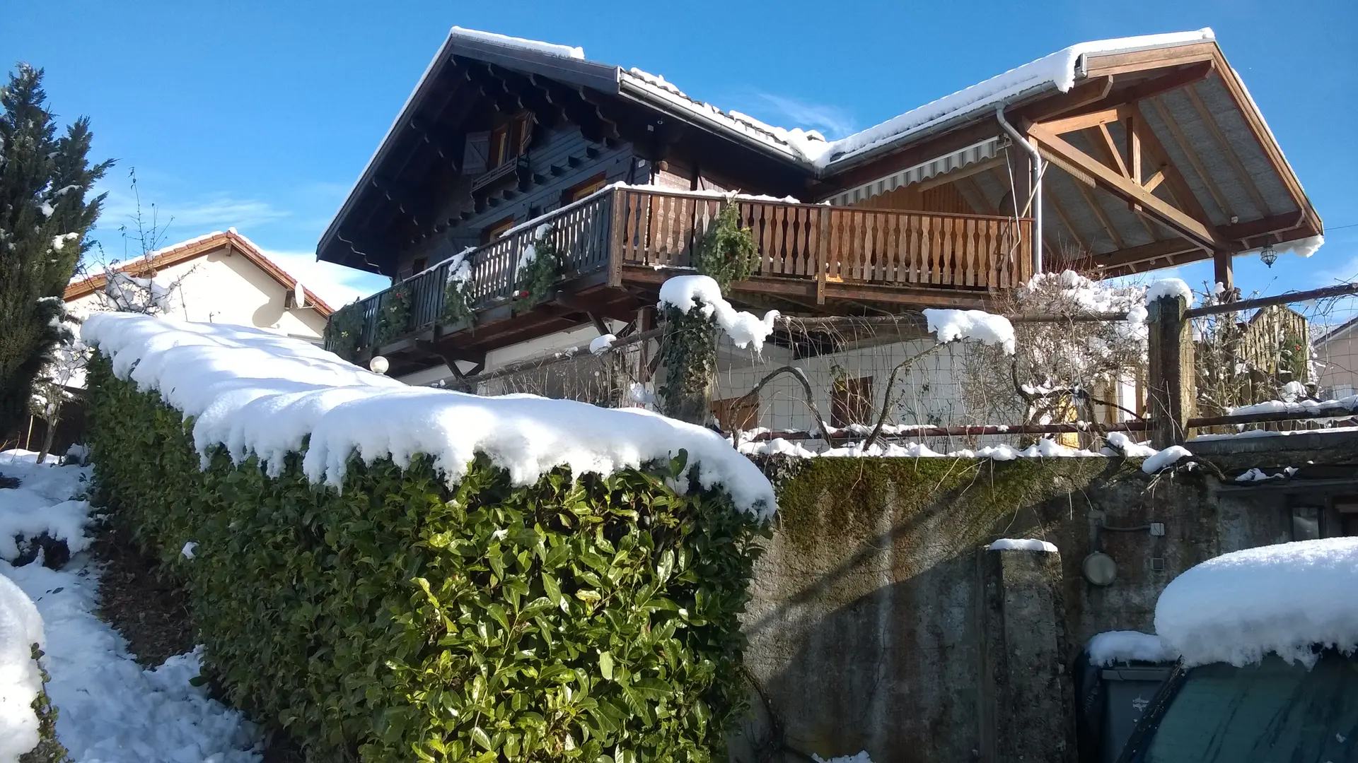 C'est une maison de style chalet, avec un toit pentu et un balcon en bois, située dans un environnement enneigé.