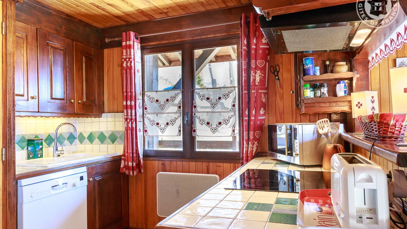 Cuisine avec fenêtre. Deux plans : côté évier, lave-vaisselle et lave-linge dans l'armoire, en face le côté cuisson