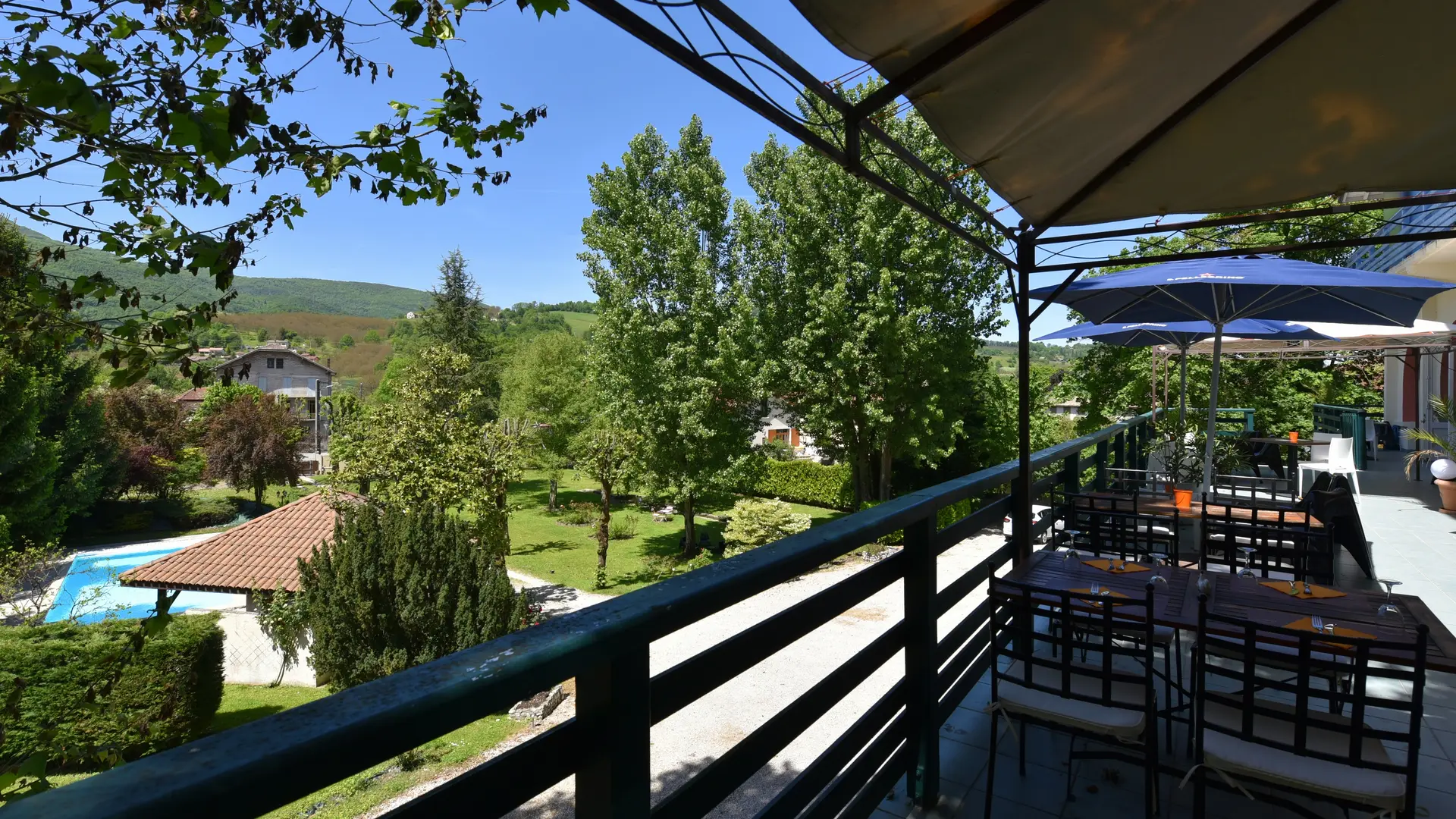 Panorama sur la terrasse, le jardin verdoyant et la piscine sous un ciel lumineux d’été