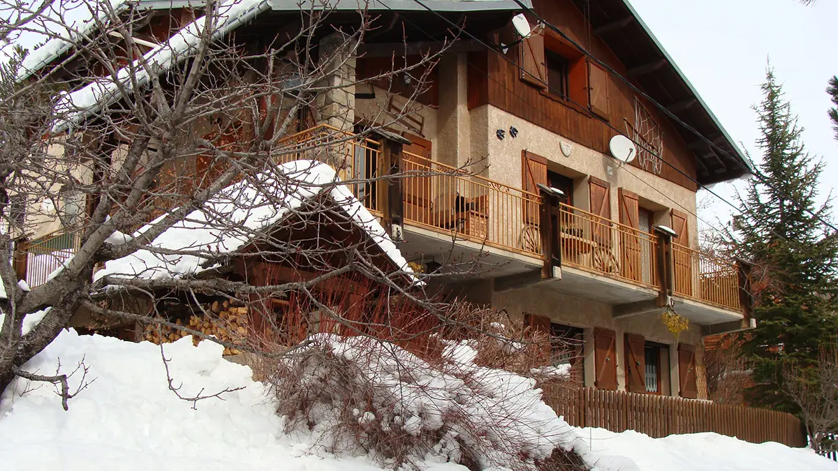 Vue de derrière d'une maison à 3 étages en bois et pierre, balcons métalliques et paysage enneigé