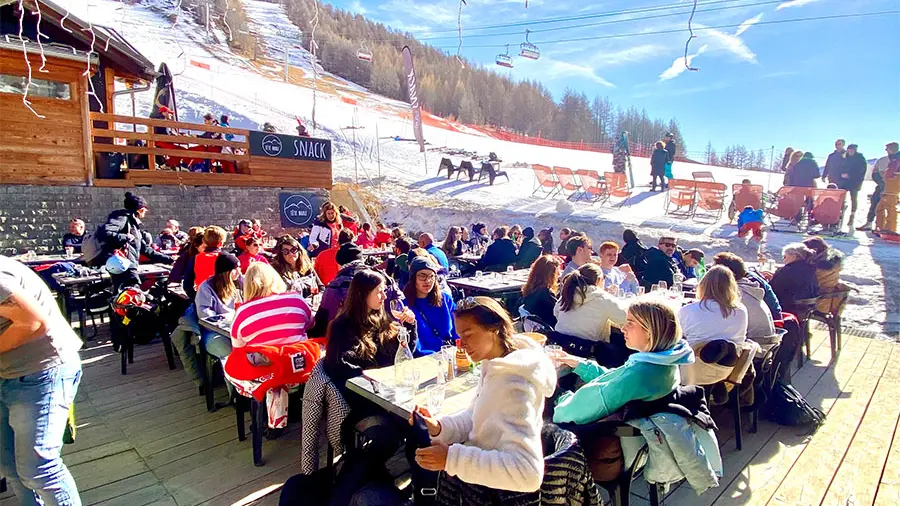 Terrasse ensoleillée du restaurant, tables et chaises, accès aux pistes enneigées, télésiège à proximité