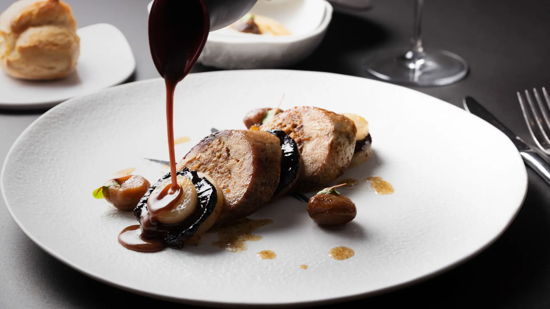 Une assiette blanche contient une préparation culinaire composée d'aliments coupés en morceaux et nappés d'une sauce foncée.