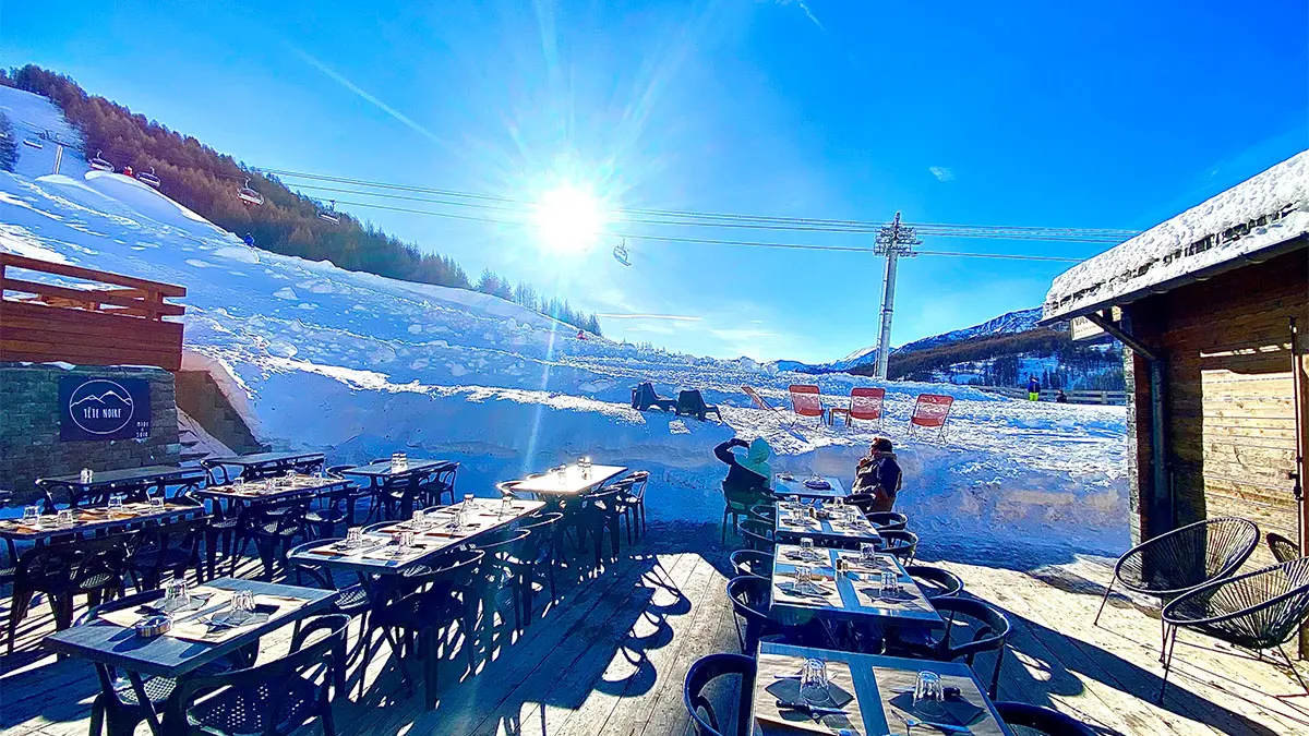 Terrasse ensoleillée du restaurant, tables et chaises, accès aux pistes enneigées, télésiège à proximité