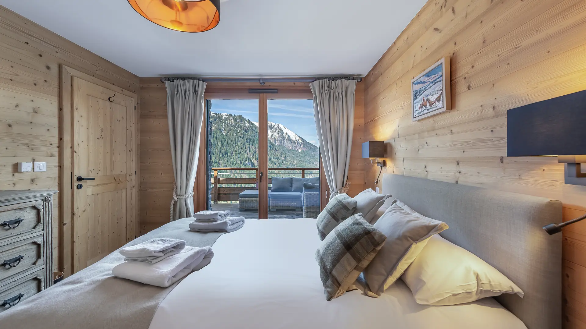 Chambre double avec grand lit, accès au balcon par une porte fenêtre, vue montagne