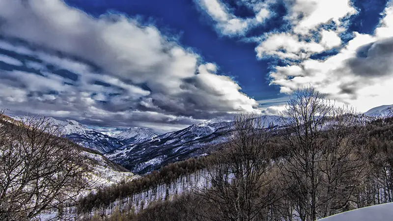 Vue des montagnes et des forêts enneigées de Val d'Allos - La Foux depuis le sentier raquettes des Grands Prés, ciel bleu en arrière-plan