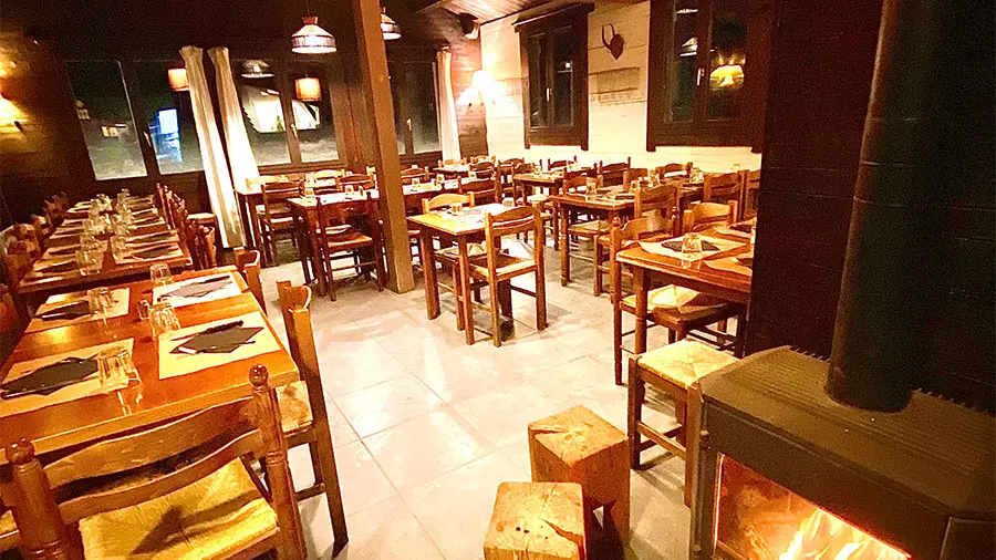 Salle intérieure du restaurant, ambiance confortable avec tables et chaises en bois, sol carrelé, poêle à bois