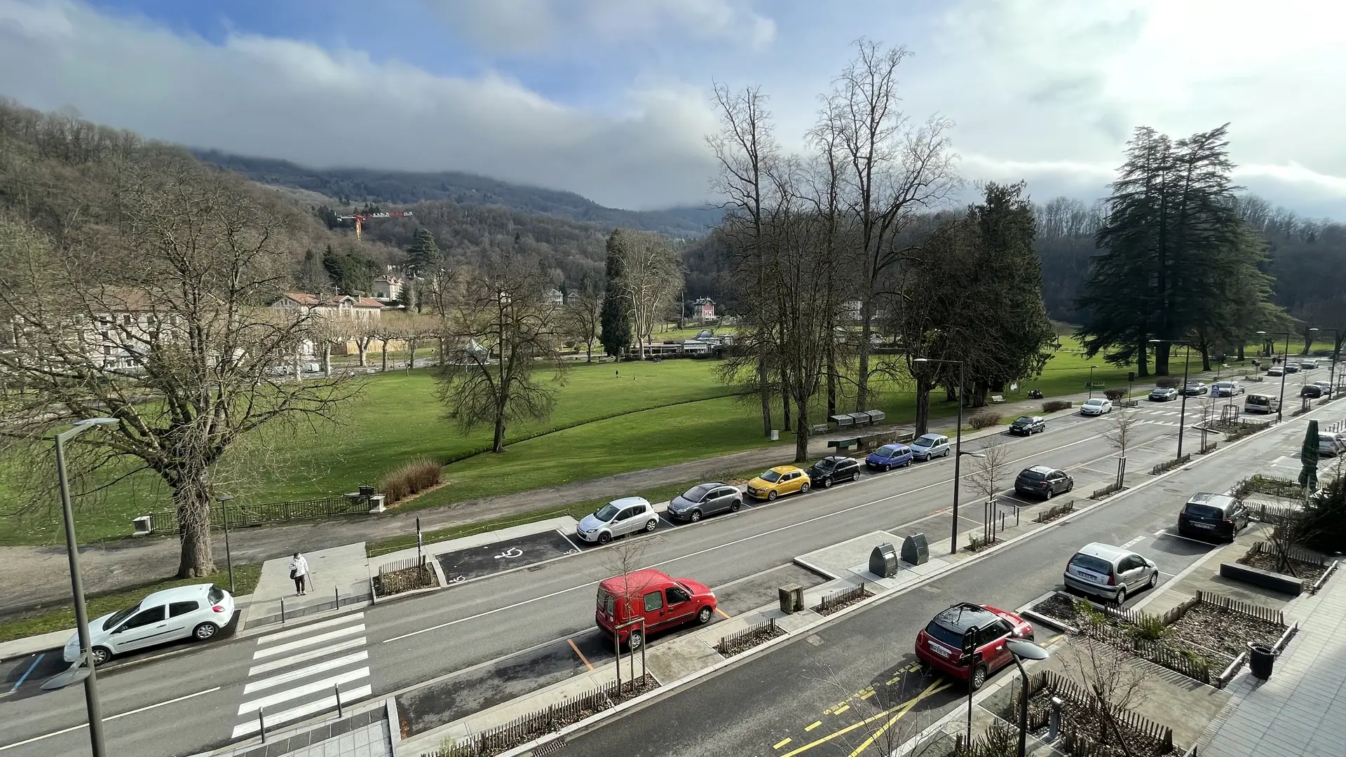 Une scène paisible de ville et de nature se dévoile, avec une rue animée contrastant avec la tranquillité du parc et des collines environnantes.