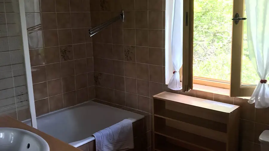 Salle de bains carrelée avec baignoire, évier, ameublement bois, fenêtre