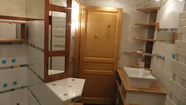 Cette salle de bains est équipée d'un lavabo simple et de nombreuses étagères en bois. Les murs sont carrelés.