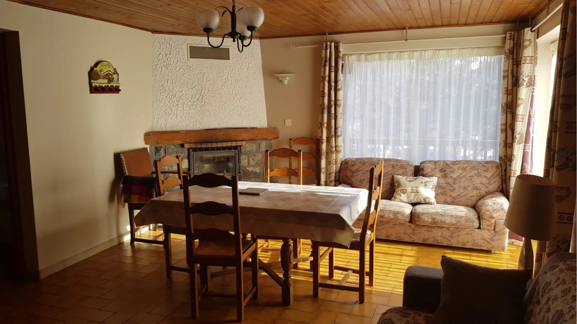 Grand salon d'appartement lumineux, avec table à manger, canapé, cheminée, fauteuil, grande fenêtre, sol carrelé