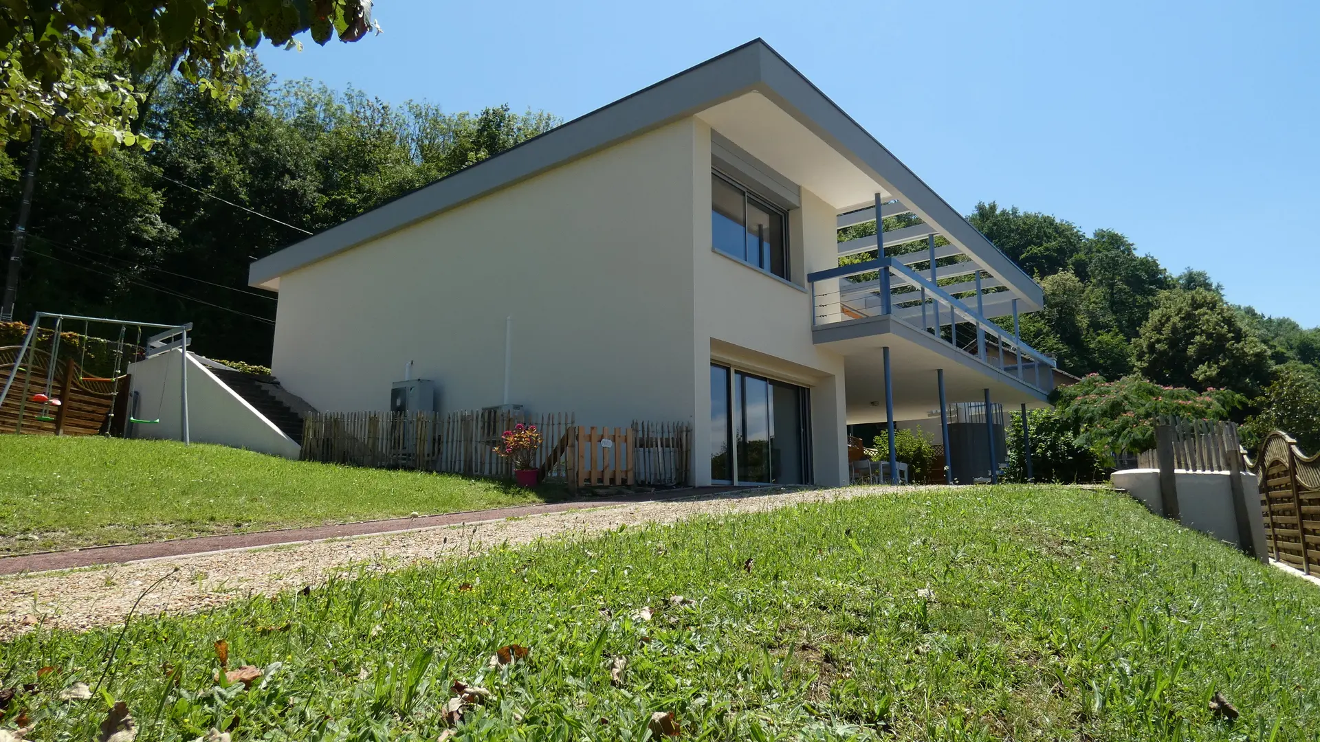 Au bout d'un chemin verdoyant, une large et grande villa moderne affiche une immense terrasse ouverte sous le ciel bleu.