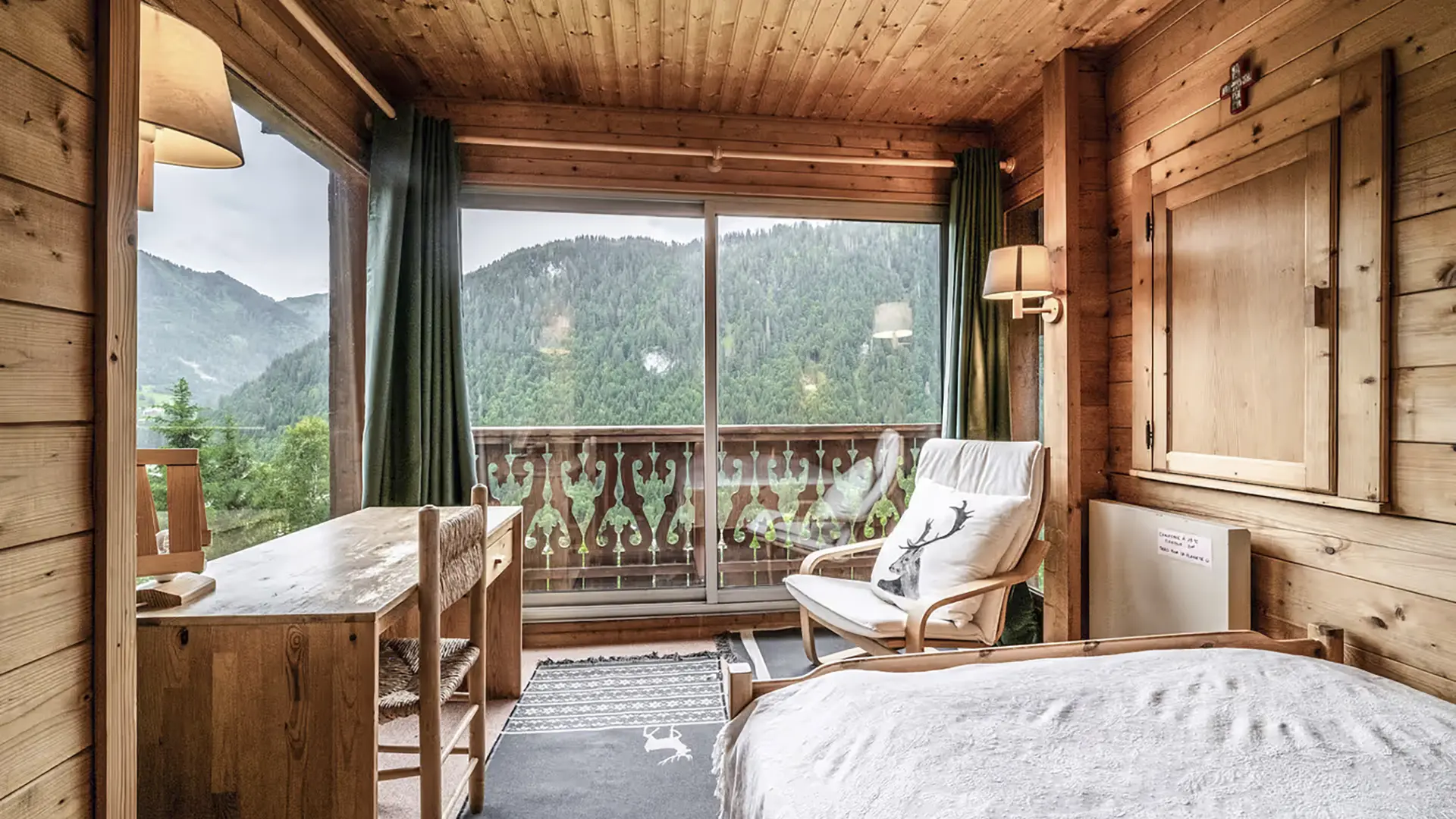 Chambre double, coin bureau, fauteuil, deux grandes baies vitrées donnant accès au balcon et vue sur les montagnes