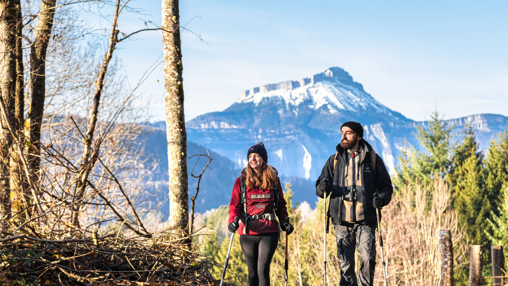 Une promenade paisible dans les bois d’un couple de randonneurs, avec une vue sur un sommet enneigé.