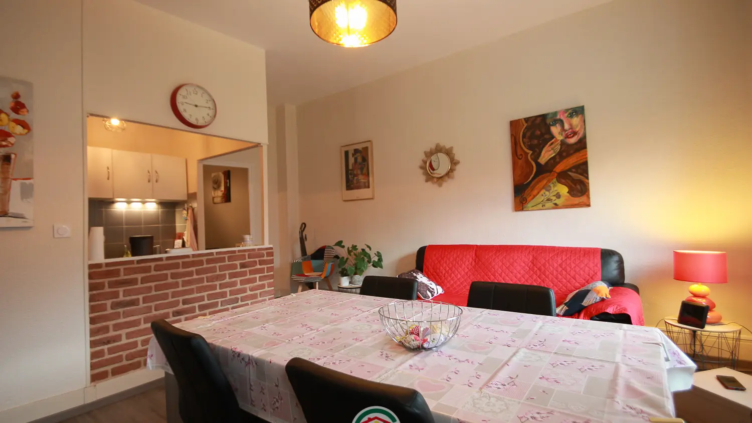 Un salon lumineux avec un canapé, une table de salle à manger et une cuisine ouverte séparée par un mur décoratif en briques.