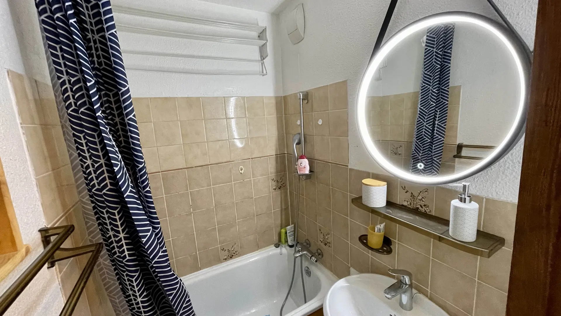 Vue d'ensemble de la salle de bain avec baignoire-douche et son rideau, lavabo et miroir