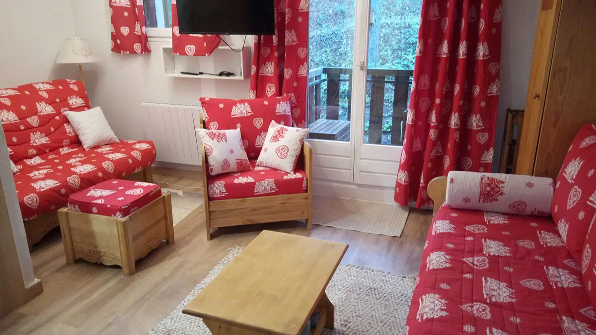 Bright studio apartment living room with sofa, armchairs, wall-mounted TV, window opening onto a balcony