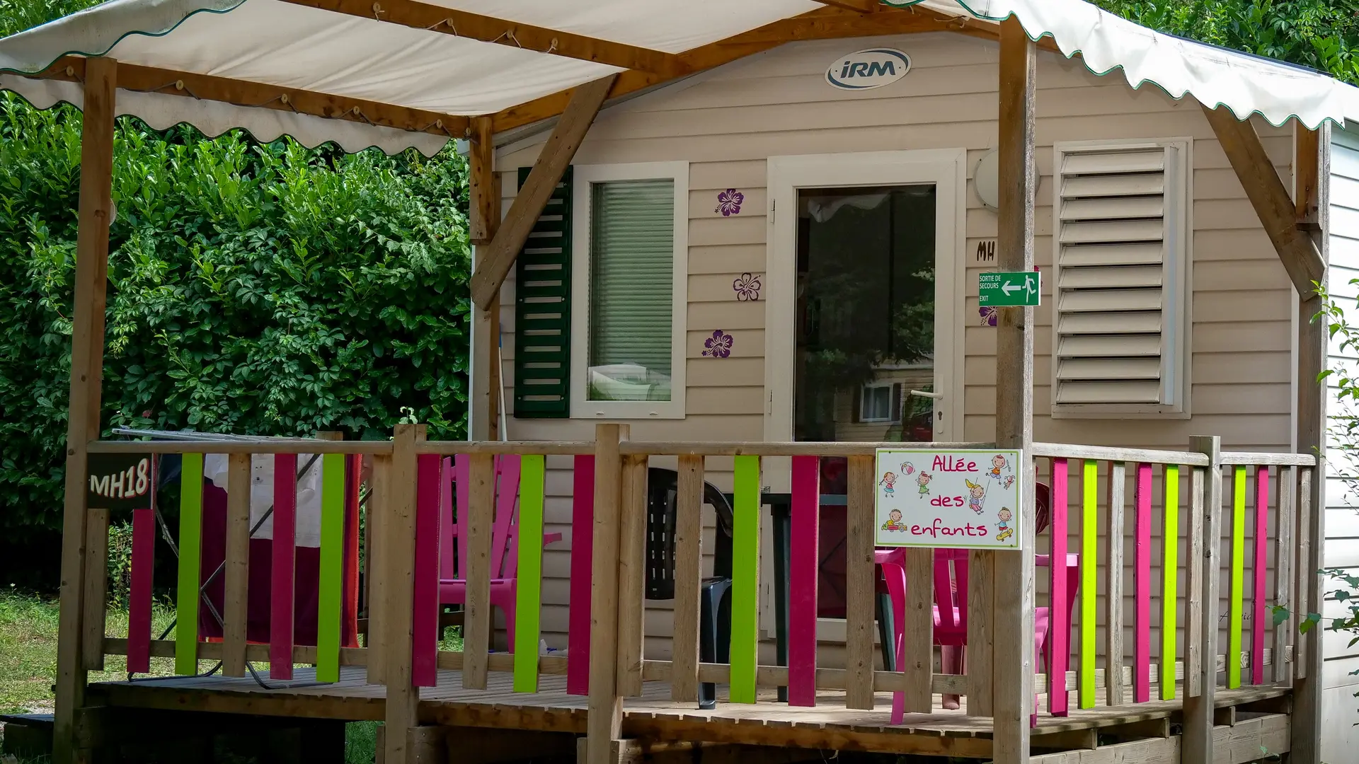 L'extérieur du mobil-home est caractérisé par une terrasse en bois une toiture en partie couverte avec une balustrade multicolore.