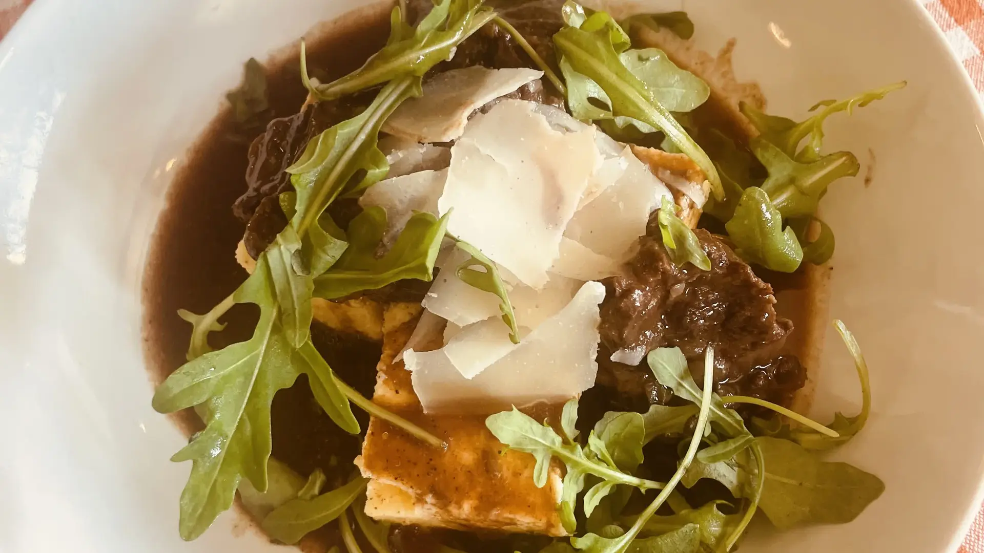 Plat savoureux garni de roquette et de copeaux de parmesan sur une nappe à carreaux rouges.