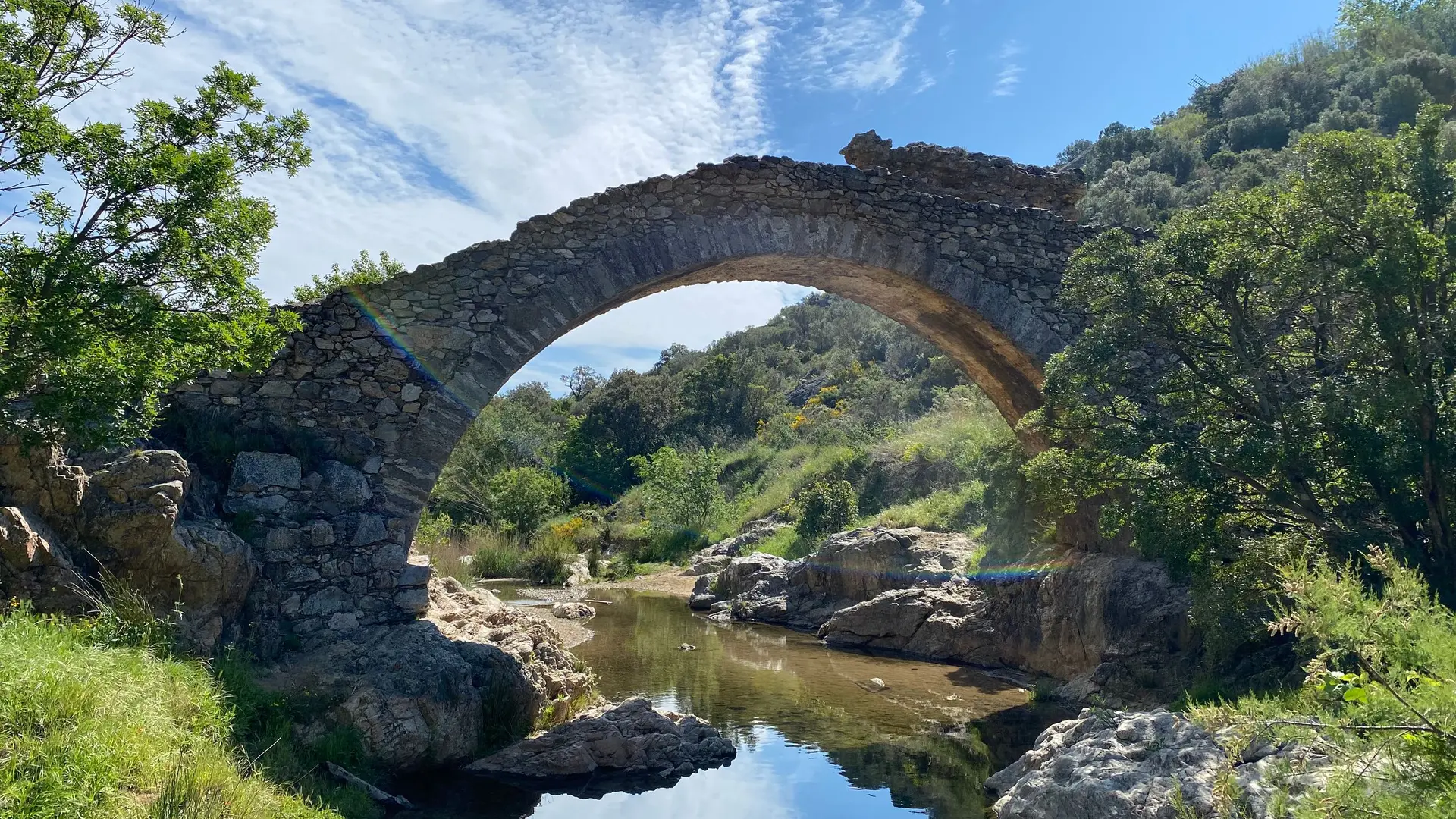 Pont en pierres apparentes enjambant une petite rivière entouré de végétation méditerranéenne