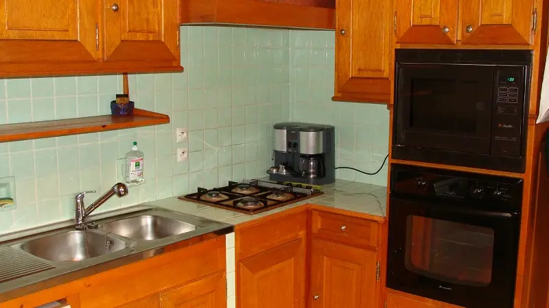 Coin cuisine avec ameublement bois, plaques de gaz, four, micro-ondes, carrelage mural