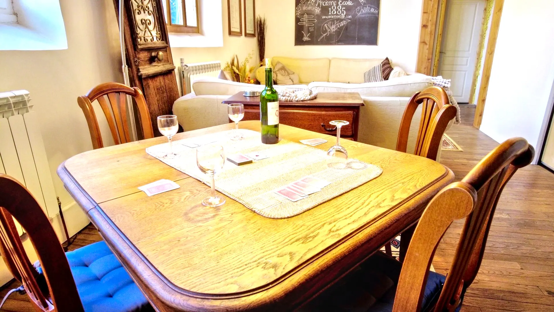 Une belle pièce de vie très lumineuse avec ses trois grandes fenêtres. Elle est toute en longueur avec plusieurs postes de loisirs,. Deux salons et entre les deux une table pour faire des jeux avec un lampadaire à arc. On trouve un poêle à bois au fond de la salle avec à gauche du poêle, un guéridon bas et une lampe avec un serviteur contenant le bois et à droite une armoire vintage peinte en blanc. A côté du canapé, on retrouve un autre guéridon et une lampe avec au-dessus un grand miroir sur le mur. Au premier plan, deux autres canapés et une table basse. en décoration, une veille porte à côté du canapé. Le lustre de la pièce est composé de plusieurs lanternes en papier blanc. Sur la gauche, un escalier en bois permet d'accéder à la mezzanine.