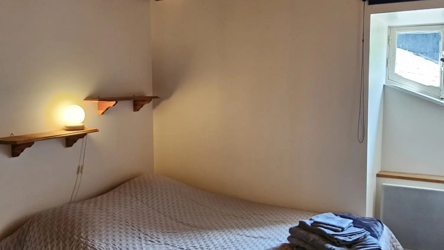 Cette chambre est simple et fonctionnelle. Un lit double occupe la majeure partie de la pièce. Une fenêtre offre une vue sur l'extérieur et apporte de la lumière naturelle. Le plafond est en bois et une lampe de chevet éclaire le coin du lit.