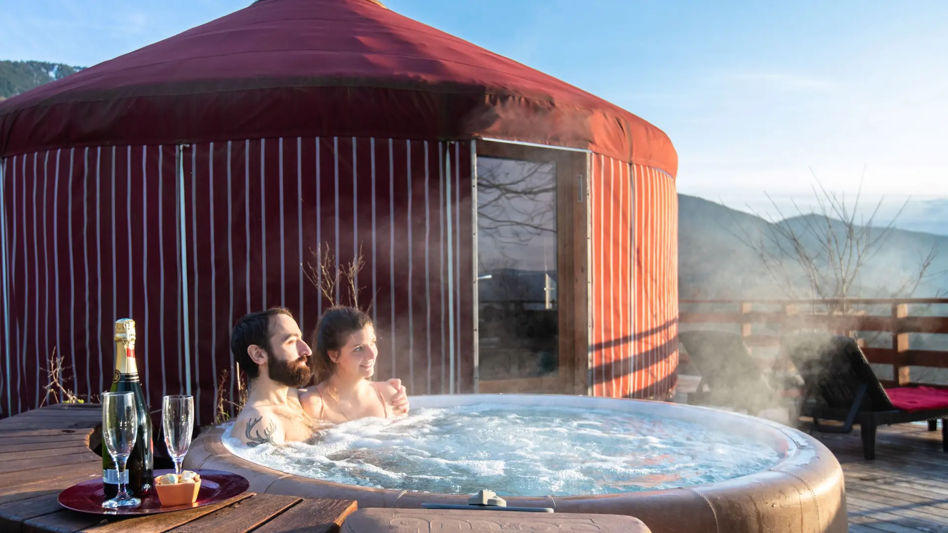 Couple dans un jacuzzi devant une yourte rouge.