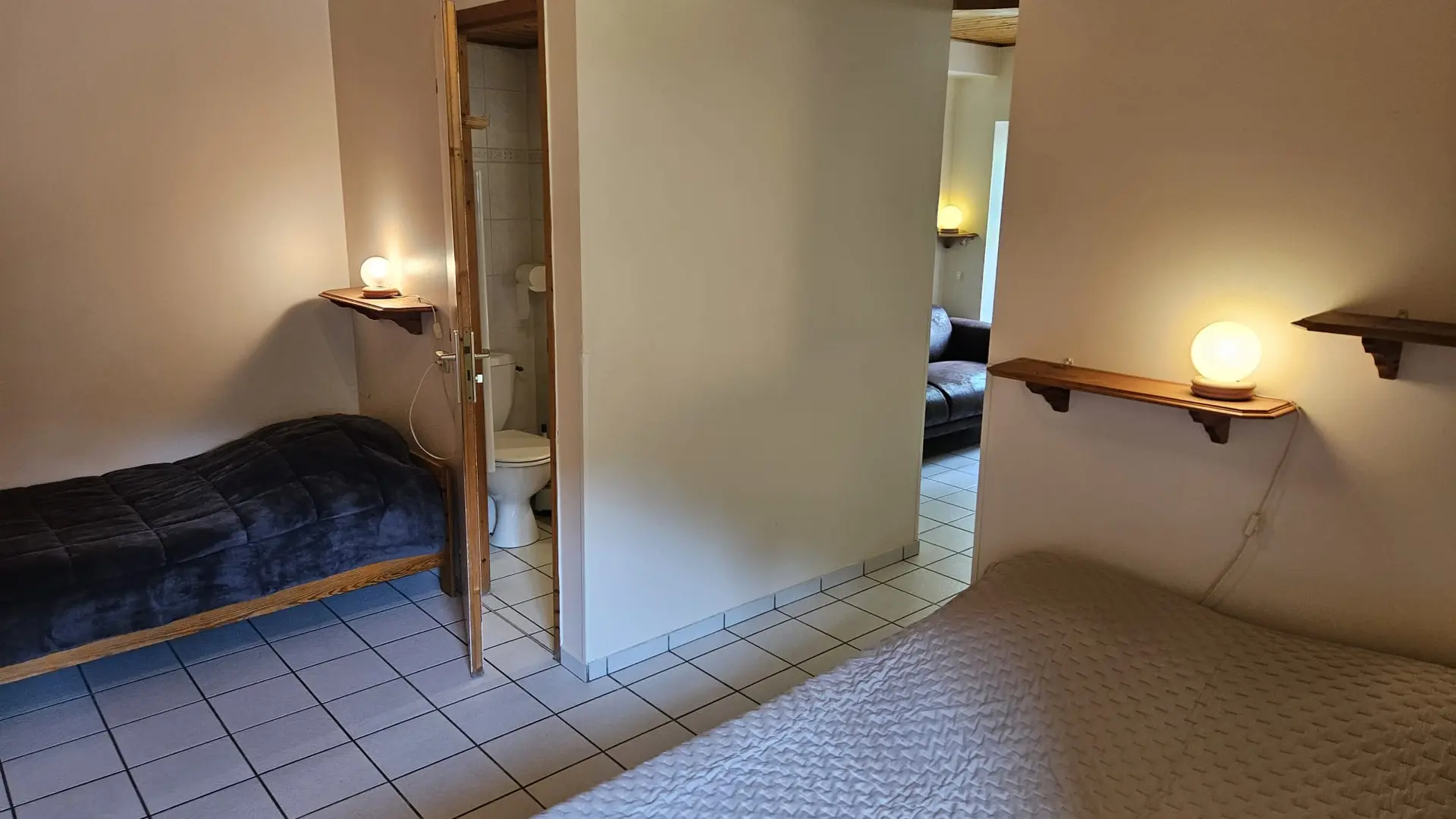 Cette chambre offre un espace nuit et un coin salon. Deux lits (un simple et un double) sont disposés dans la partie nuit, séparée du salon par un couloir.