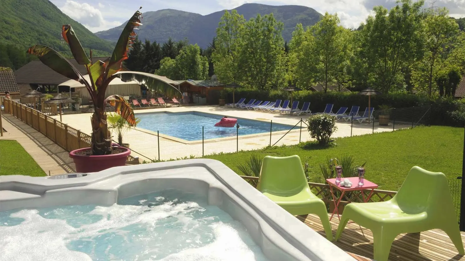 Un bain à remous bouillonnant se trouve au premier plan, entouré de chaises longues et d'une piscine, avec une vue sur les montagnes en arrière-plan.