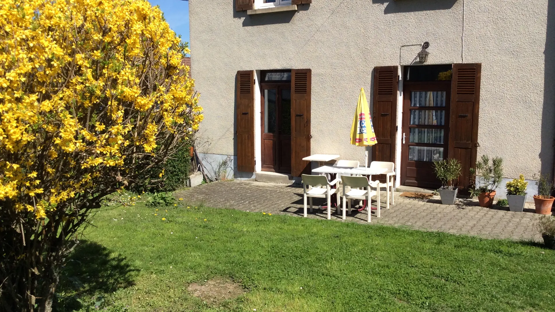 L'extérieur de la maison avec une table de jardin en plastique blanc pour 4 personnes.