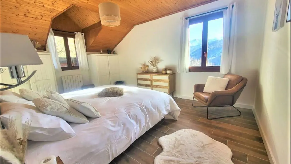 Chambre à coucher lumineuse avec lit double, ameublement bois, parquet au sol, fenêtres donnant sur les montagnes