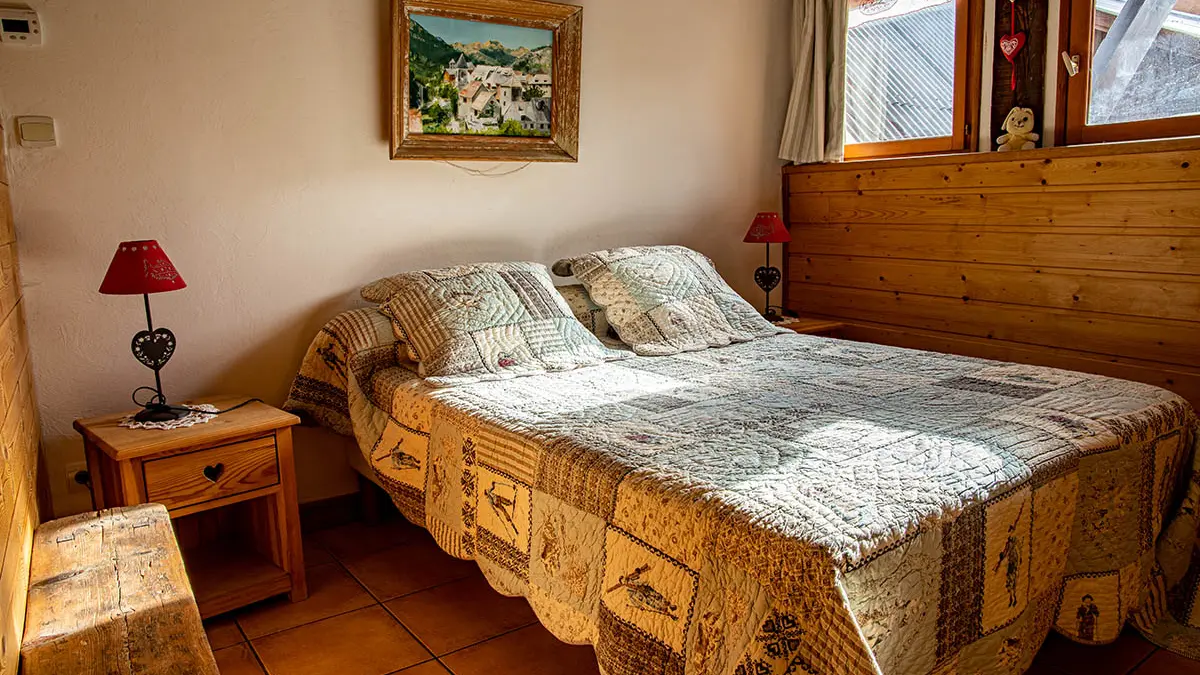 Bright bedroom with double bed, wooden furniture and windows overlooking the village