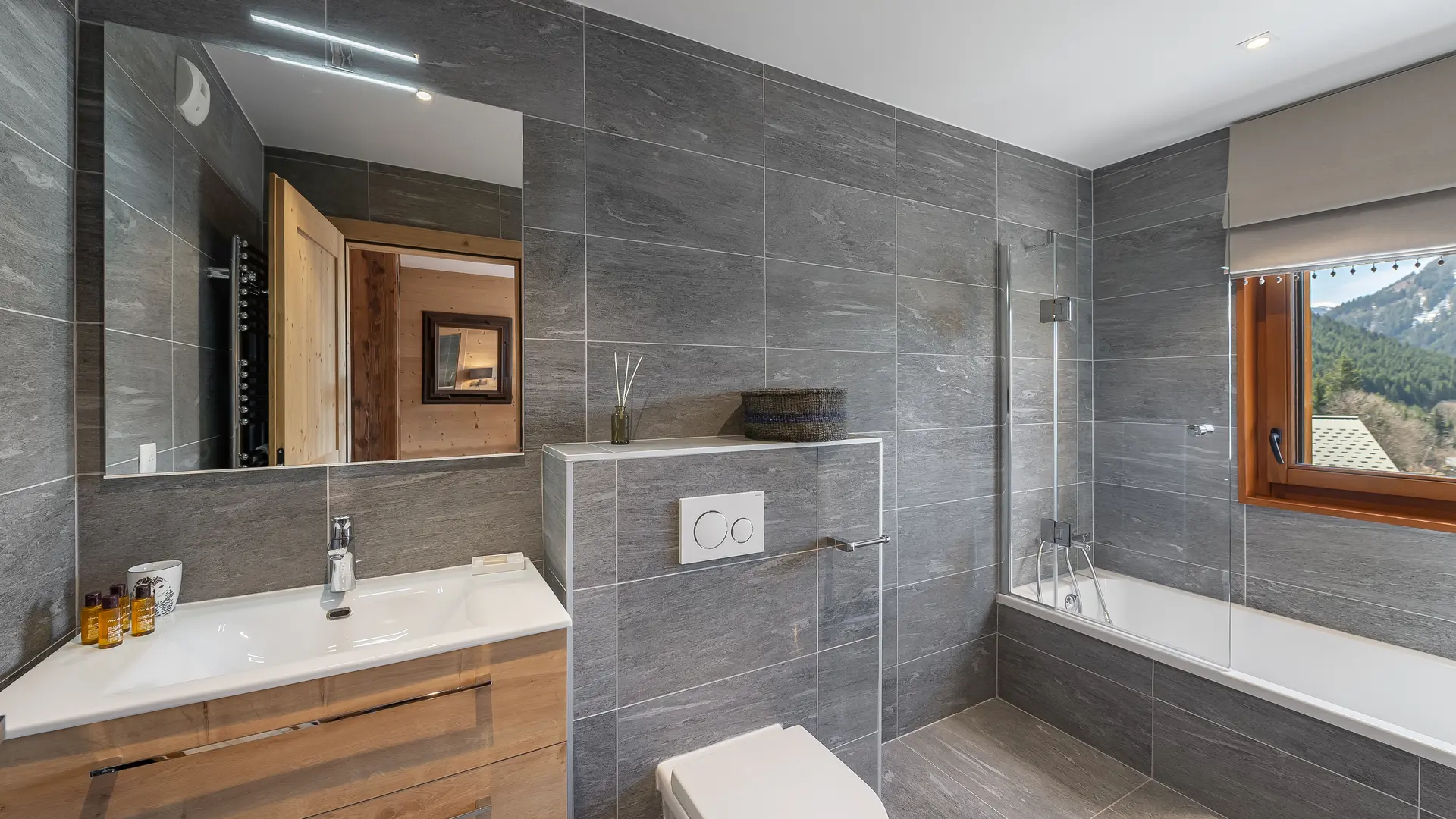 Salle de bains avec baignoire, toilettes, vasque et son meuble, grand miroir, fenêtre