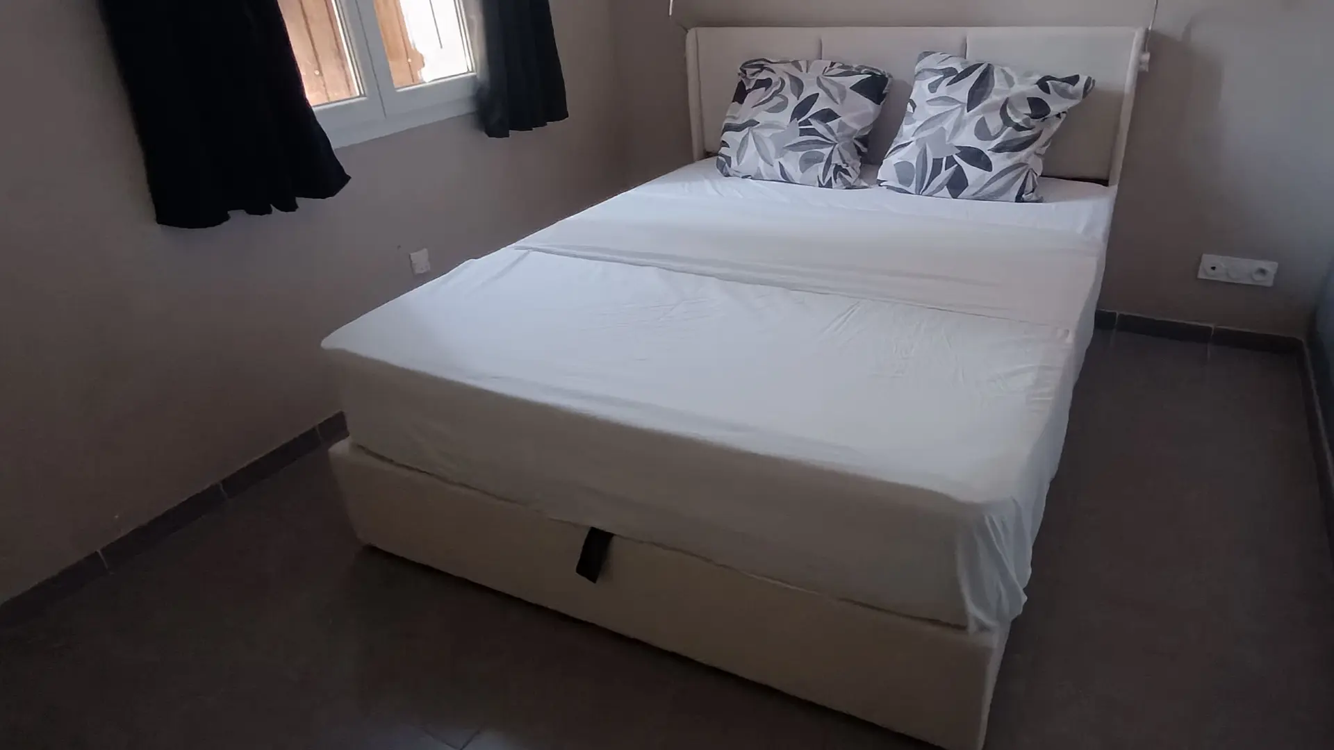 Chambre double avec lit confortable, tête de lit capitonnée, télévision murale et table de chevet.