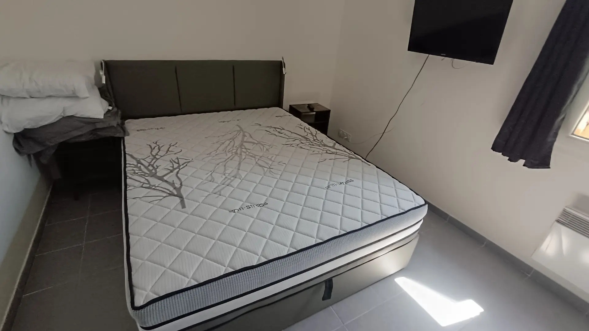 Chambre équipée d’un lit double avec tête de lit rembourrée, deux oreillers décoratifs et une fenêtre apportant de la luminosité naturelle.