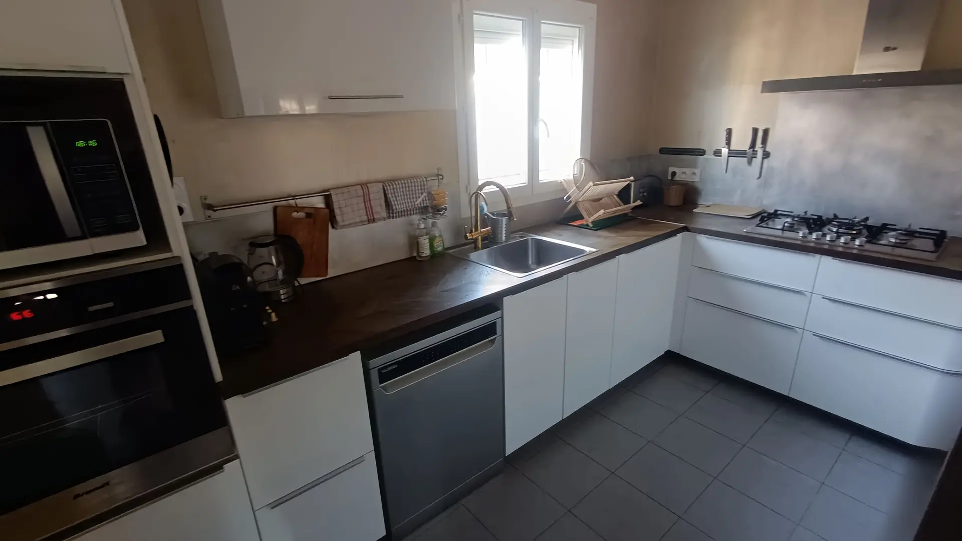 Cuisine spacieuse avec plan de travail fonctionnel, plaque de cuisson gaz, hotte et grand réfrigérateur-congélateur.