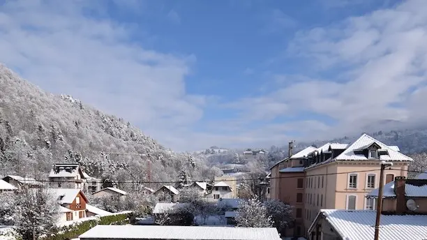 Un paysage hivernal enneigé avec une vue sur les toits d’Uriage et les collines environnantes.