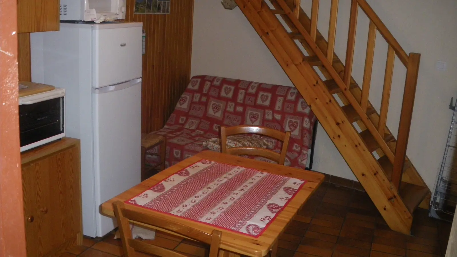 Coin séjour et cuisine avec table à manger, canapé, four à micro-ondes, TV, ameublement bois et parquet au sol, escalier vers l'étage supérieur