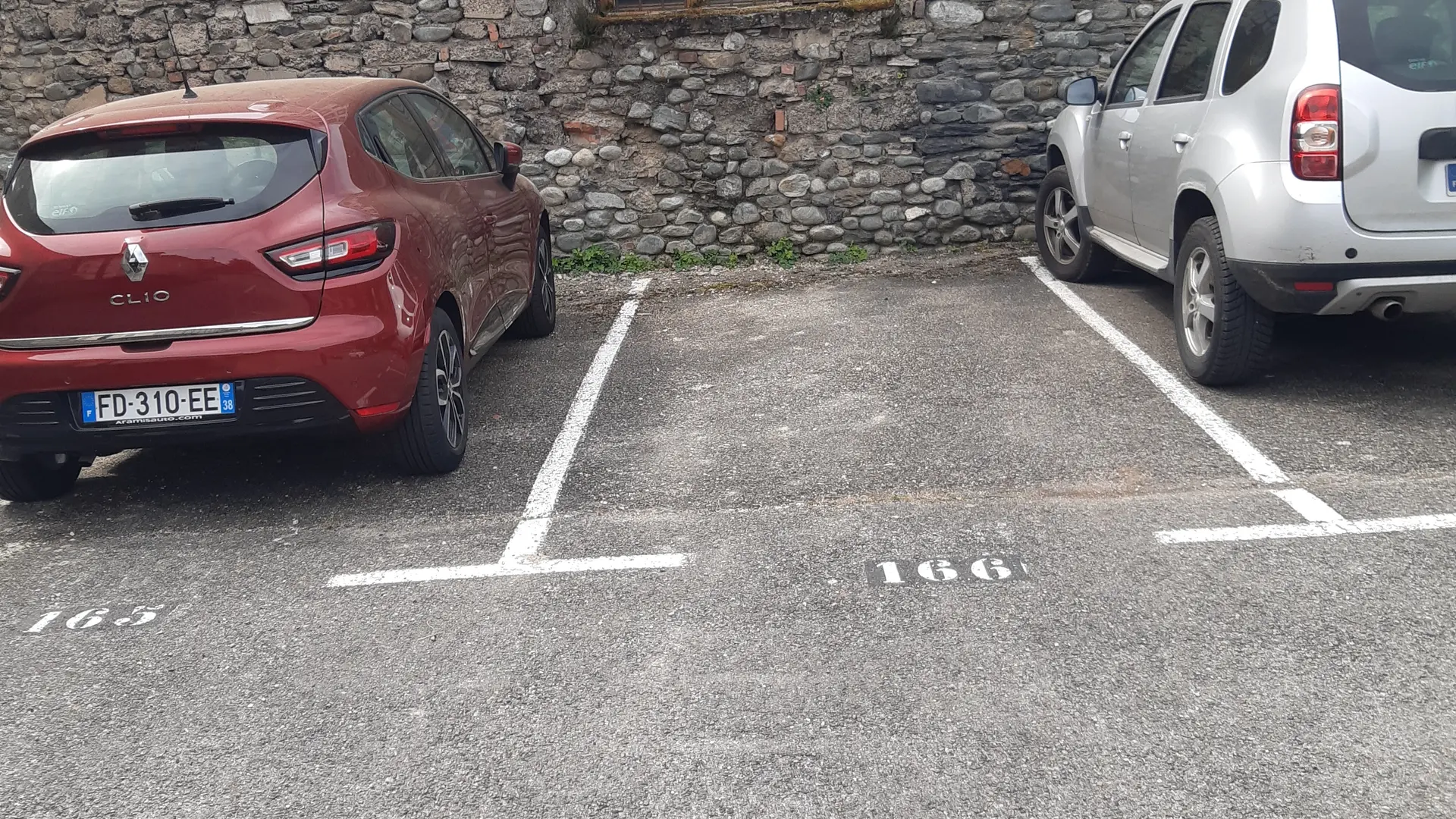 Deux véhicules stationnés dans un parking, alignés sur des places marquées,.