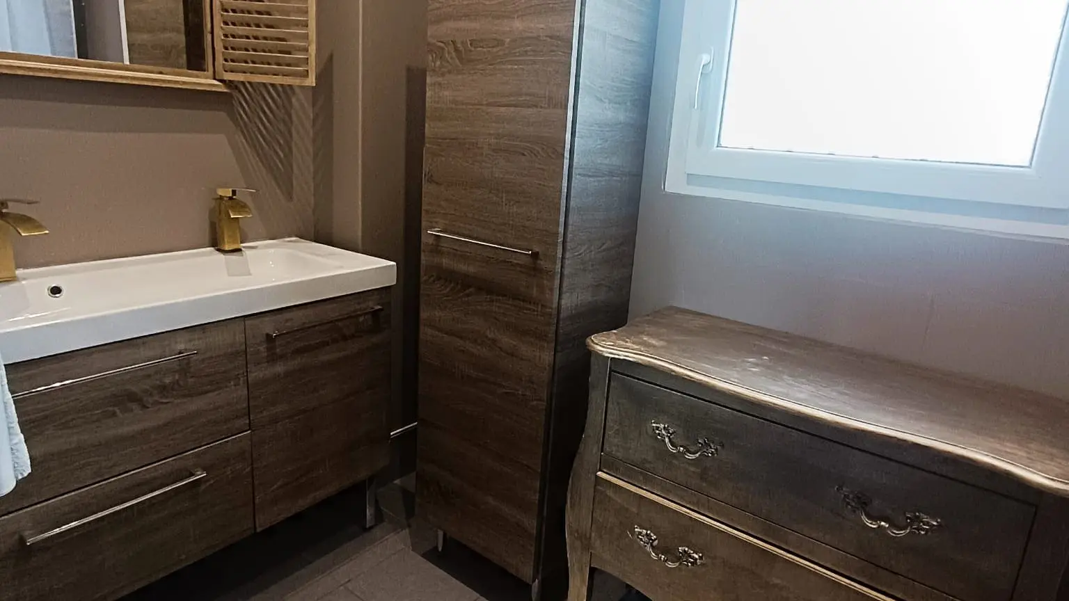 Salle de bain équipée d’un meuble double vasque, rangements modernes et fenêtre avec lumière naturelle.