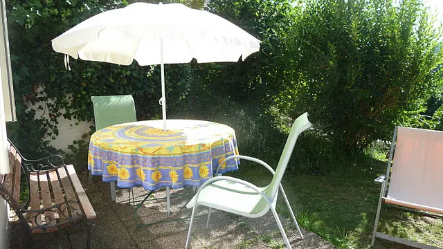 Un coin paisible aménagé en plein air avec un salon de jardin composé d'une table et de chaises. Un parasol apporte de l'ombre à cet espace vert.