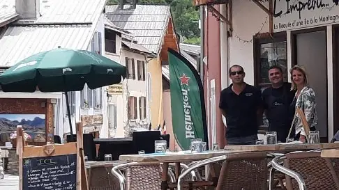 Terrasse extérieure du restaurant dans la grand-rue d'Allos, fausse pelouse, tables et chaises, parasols