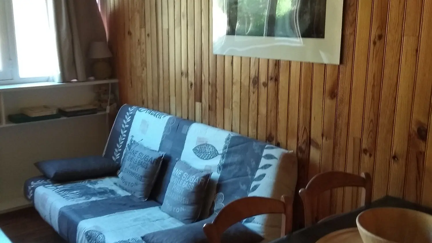 Séjour lumineux avec ameublement bois, lambris, canapé, fenêtre et rideaux