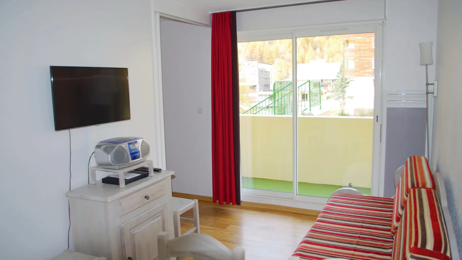 Bright living room with sofa, TV, french window, balcony and curtains