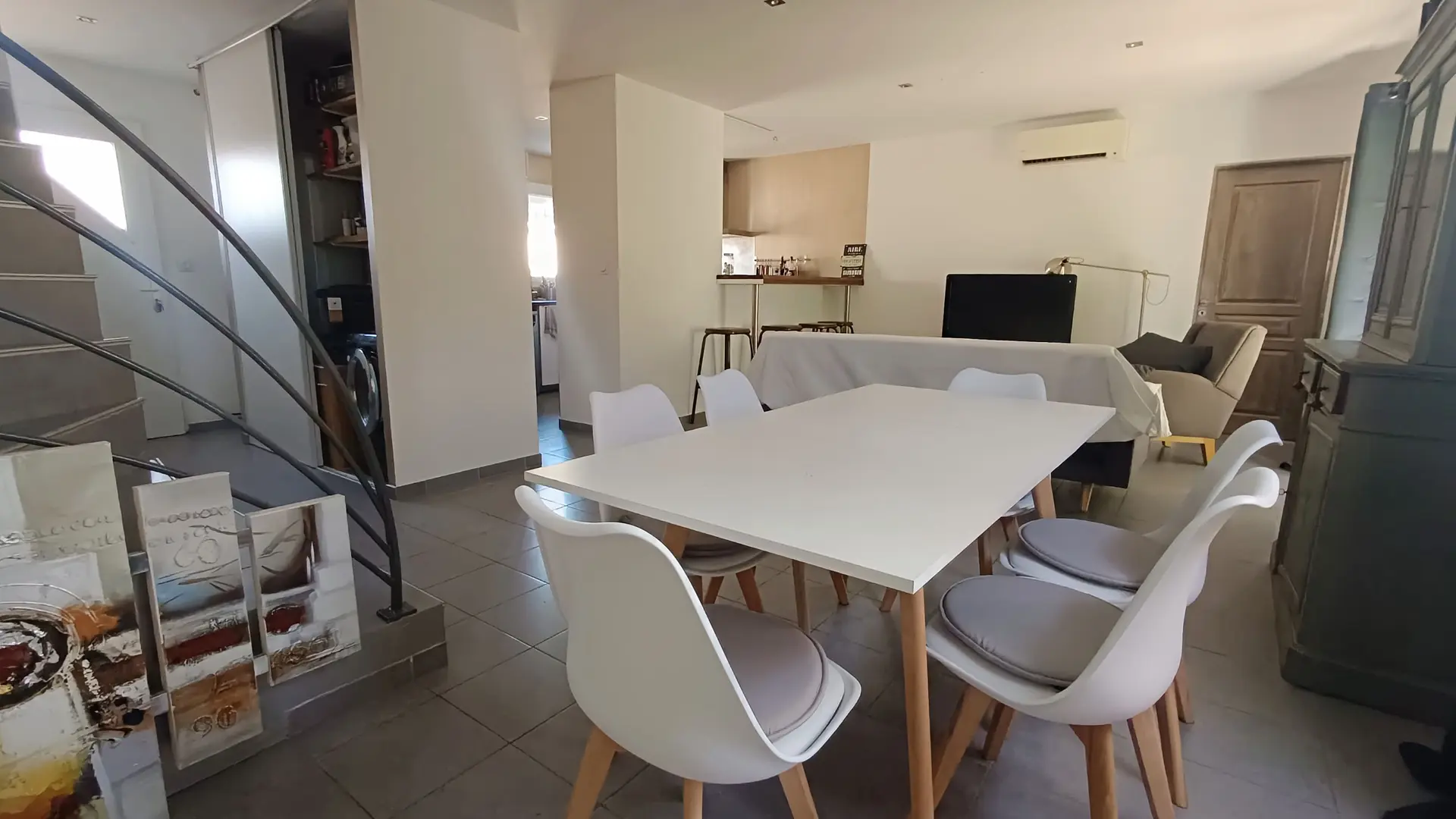 Séjour spacieux avec grande table à manger, coin salon et escalier donnant accès à l’étage.
